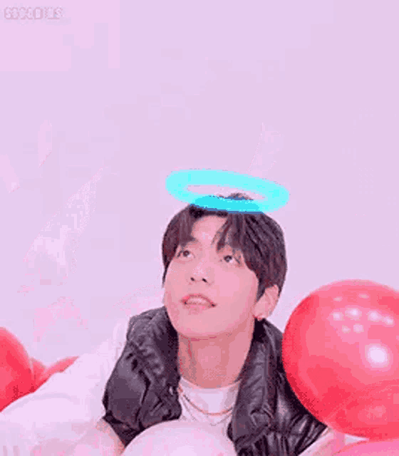 a man is sitting in a pile of pink and red balloons with his hand up .