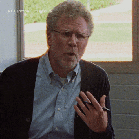 a man wearing glasses and a cardigan is talking in front of a window with la guarimba film festival written on the bottom