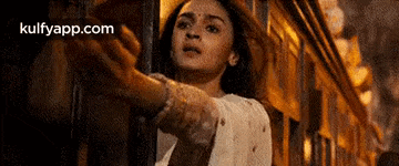 a woman in a white dress is standing next to a train and reaching out towards it .