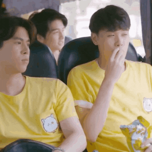 a group of young men are sitting on a bus and one of them is eating a snack .