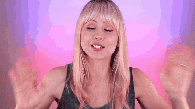 a woman with blonde hair is making a funny face with her eyes closed and her hands in the air .