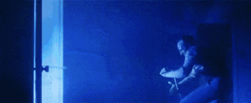 a man is standing in a doorway in a dark room with a blue light coming out of it .