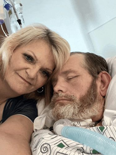 a man with a beard is laying in a hospital bed with a woman