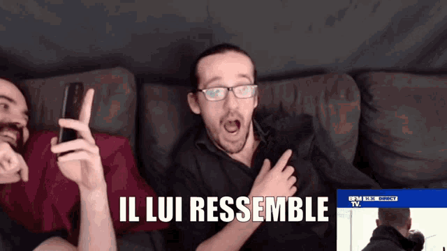 two men are sitting on a couch and one of them is holding a cell phone and says il lui ressemble