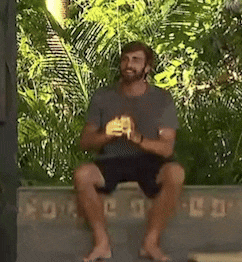 a man with a beard is sitting on a bench with his legs crossed and holding something in his hands .