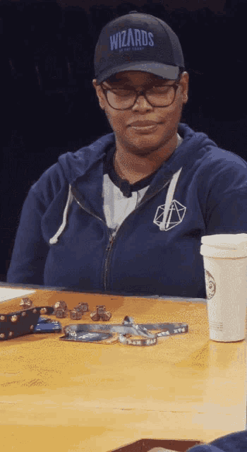 a woman wearing a wizards baseball cap sits at a table
