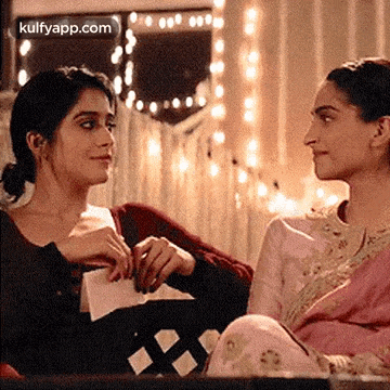 two women are sitting at a table talking to each other .