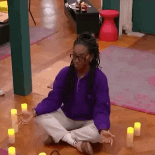 a woman in a purple sweater is sitting on the floor with her legs crossed in front of candles .