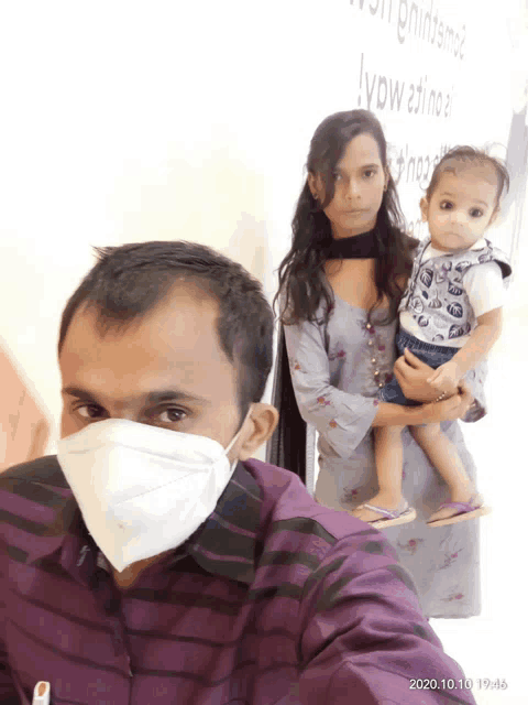 a man wearing a face mask holds a baby while a woman holds another baby
