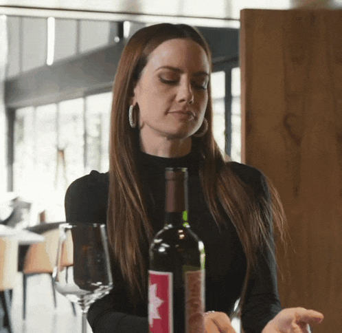 a woman holding a bottle of wine with a red label