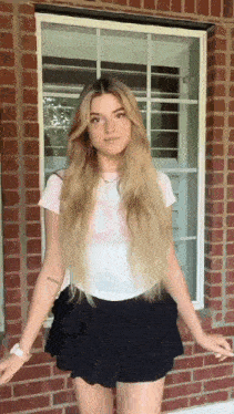 a young woman in a white shirt and black skirt is standing in front of a brick wall .