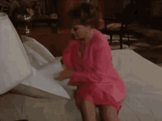 a woman in a pink jacket is sitting on a bed holding a pillow .