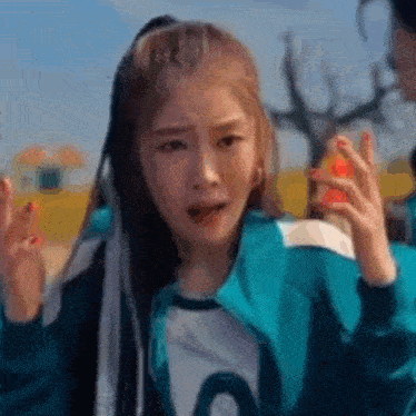 a woman in a blue jacket is making a funny face while playing squid game .