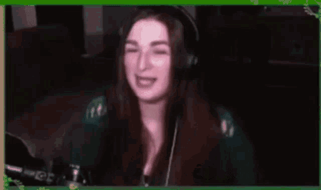 a woman wearing headphones is waving her hand in front of a green frame that says h