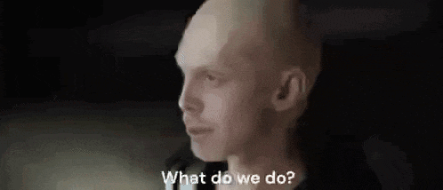 a bald man is talking to another man in a dark room and asking what do we do .