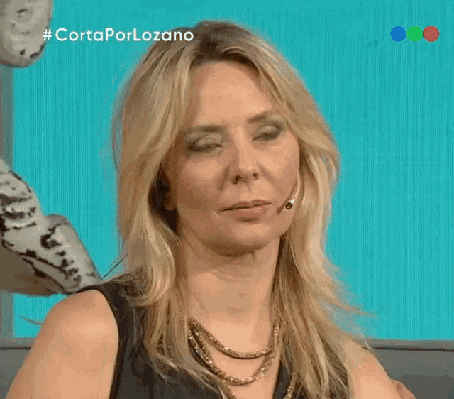 a woman is smiling in front of a blue background with # cortaporlozano on it