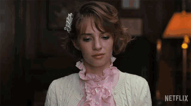 a woman wearing a pink ruffled blouse and a white sweater with netflix written on the bottom