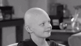 a young boy with a bald head is sitting in a chair and smiling .