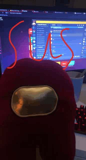 a red among us stuffed animal is sitting in front of a computer screen