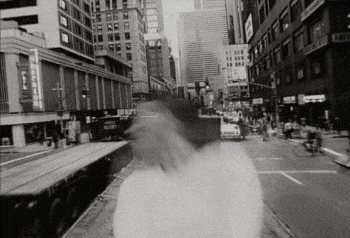 a black and white photo of a city street with a train going down the tracks .