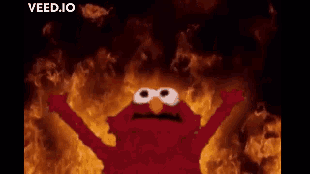 elmo from sesame street is standing in front of a fire with his arms in the air .