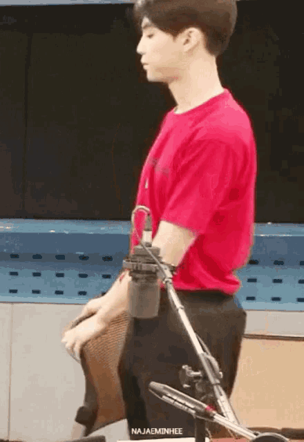 a man in a red shirt is standing in front of a microphone with the name najaeminhee written on the bottom