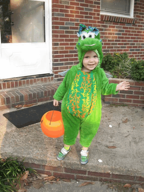 a little boy dressed in a frog costume is holding an orange bucket