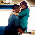 a man and a woman are hugging each other in a room . the woman is wearing a blue shirt .