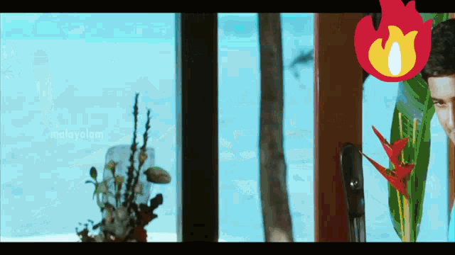 a man is standing in front of a window with a malayalam logo on the bottom