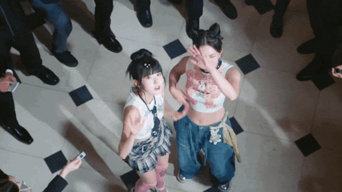 a group of people are standing around two girls one of whom is wearing a crop top with a teddy bear on it