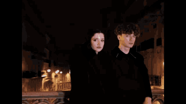 a young man with curly hair wearing a black shirt looks at the camera