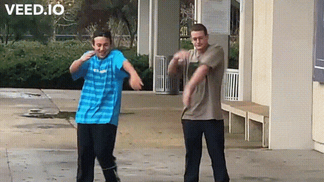 two men are dancing in front of a building that says veed.io on the top