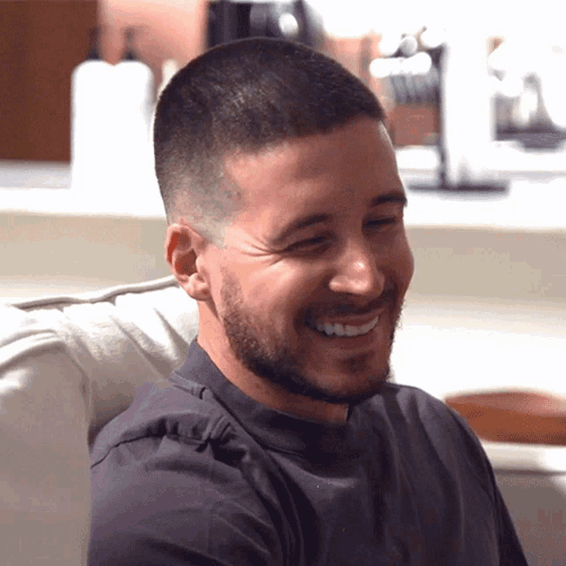 a man with a beard is sitting on a couch smiling