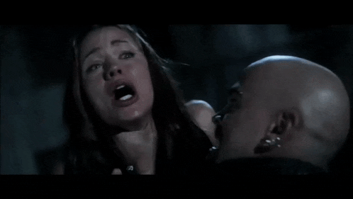 a woman is being choked by a bald man in a movie