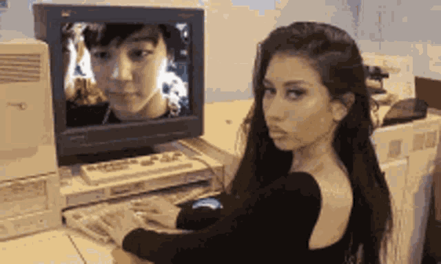 a woman sits at a desk in front of a computer monitor