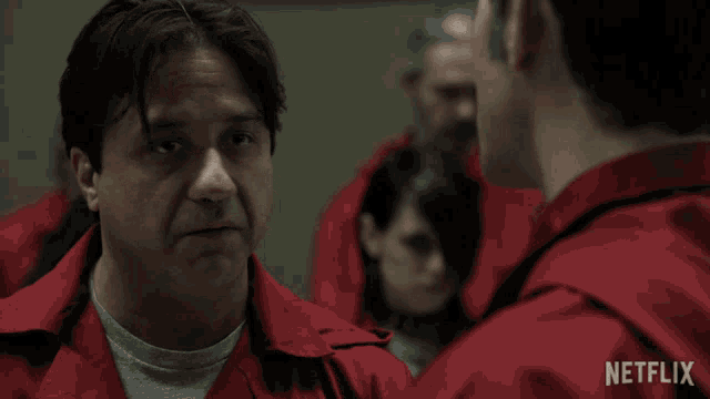 a man in a red jumpsuit is talking to another man with a netflix logo in the corner