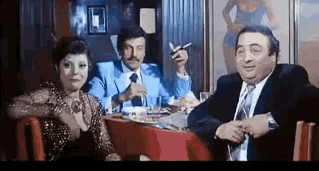 a man in a suit and tie is smoking a cigarette while sitting at a table with a woman .