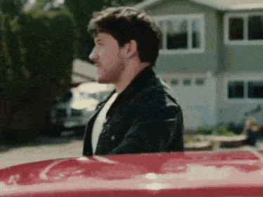 a man is standing next to a red car in front of a house .