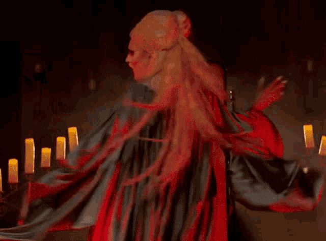a woman in a vampire costume stands in front of candles in a dark room