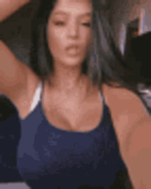 a woman in a blue tank top is taking a selfie with her arm in the air .