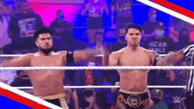 two wrestlers are standing in a ring with their arms outstretched in front of a crowd .