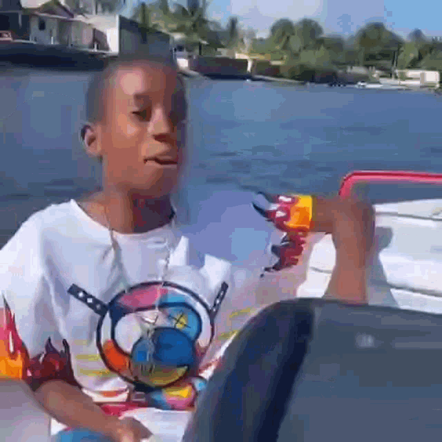 a young boy is sitting on a boat in the water and looking at the camera .