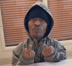 a man wearing a hooded jacket and a black hat gives the middle finger