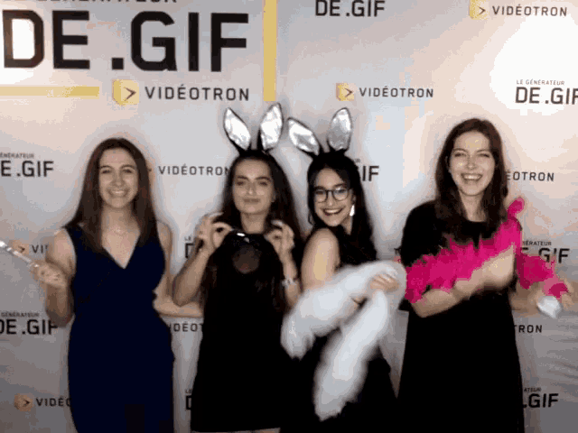 four women pose in front of a wall that says de.gif on it