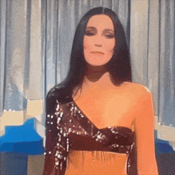 a woman with long black hair is wearing a sequined crop top .