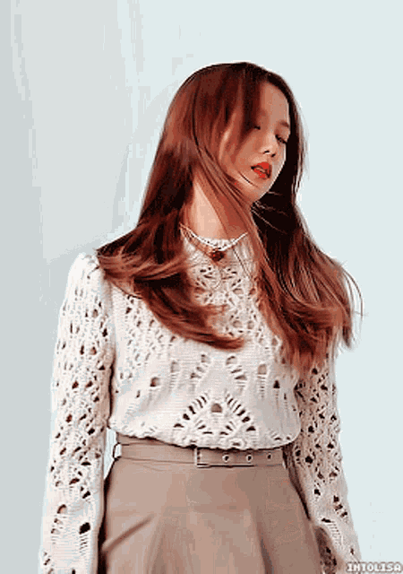 a woman wearing a white lace top and a brown skirt has her eyes closed and her hair blowing in the wind