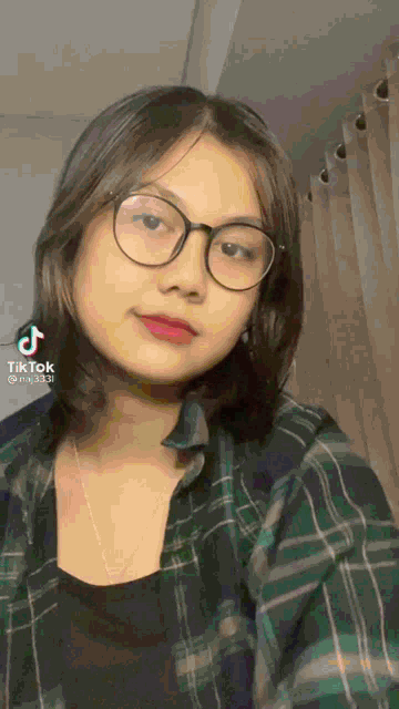 a girl wearing glasses and a plaid shirt is looking at the camera