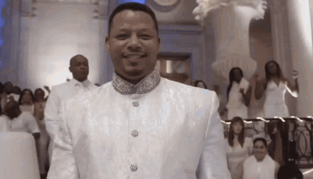 a man in a white suit is standing in front of a crowd of people