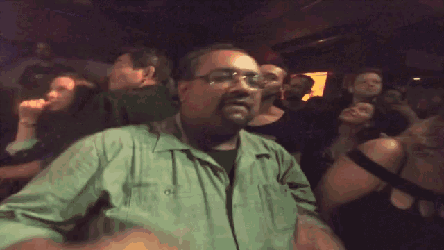 a man wearing glasses stands in a crowded room