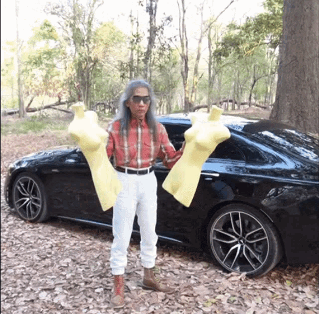 a man in a plaid shirt is holding two yellow mannequins in front of a black car